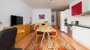 Een ruimtelijk ingerichte leefruimte met een eethoek, kitchenette en televisie.