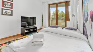 Habitación de hotel moderna con una cama grande, un televisor de pantalla plana, una mesita pequeña y un ventanal con vistas a árboles.