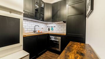 Une cuisine de taille réduite avec des meubles de couleur sombre, un crédence en carreaux blancs et un plan de travail en bois.