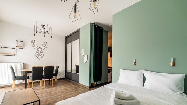 Een hotelkamer met een bed, een bureau met stoelen, een wandlamp en een schuifdeur naar een badkamer.