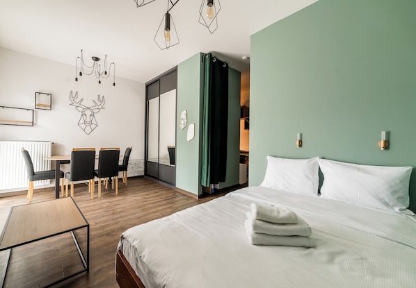 Habitación de hotel con cama, escritorio con sillas, lámpara de pared y puerta corrediza que da a un baño.