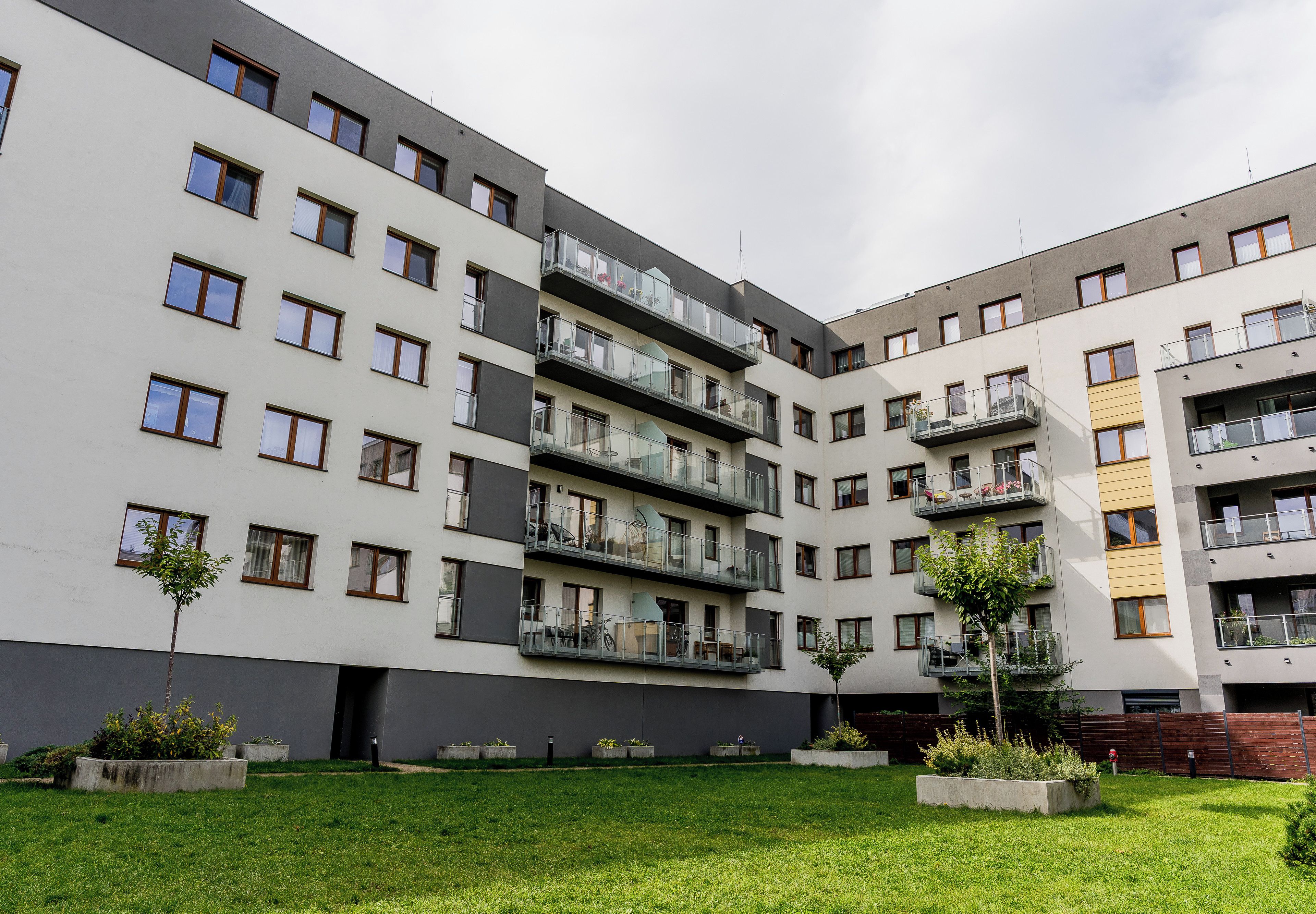 A multi-story residential building with balconies, a courtyard with grass, and concrete planters.