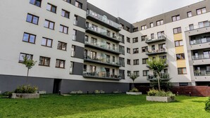 Een meerlaags woongebouw met balkons, een binnentuin met gras en betonnen plantenbakken.