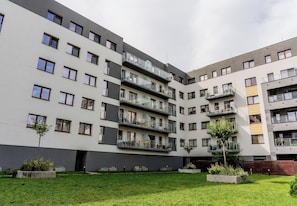 Un edificio residencial de varios pisos con balcones, un patio con césped y macetas de concreto.