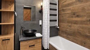 Een moderne badkamer met een houten wastafelmeubel, een zwart wastafelbakje, een witte badkuip en een douchegordijn.