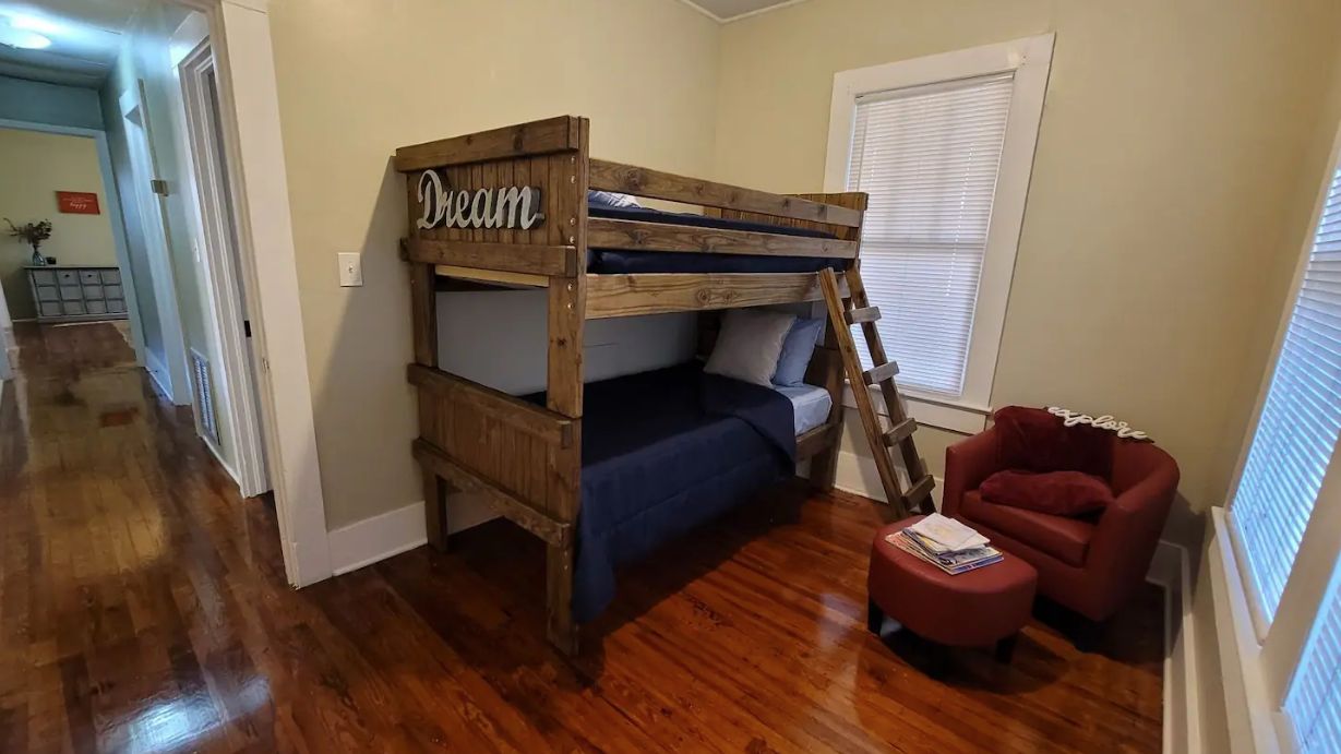 Una cama individual superpuesta con un cartel que dice 'Sueño', una silla roja y un suelo de madera.