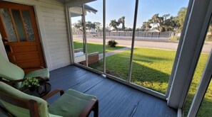 A covered porch with a view of a parking lot and a grassy area.