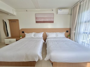 A hotel room with two beds, a wooden headboard, a small bedside table with a plant, a wall-mounted air conditioner, and a window with curtains. - Royal Oceancrest Panglao 1 (Dauis)