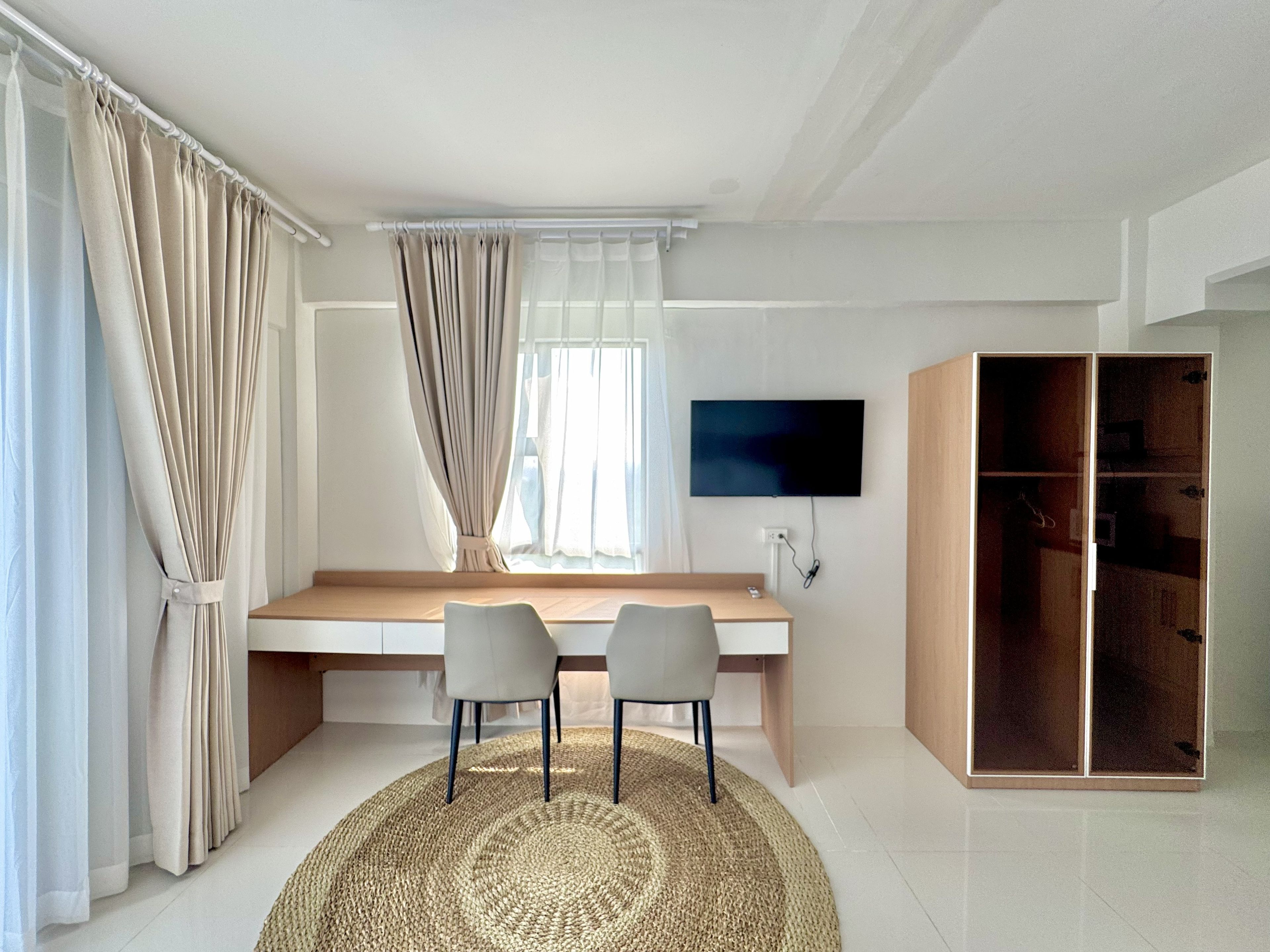 A modern room with a large window, a flat-screen TV mounted on the wall, a wooden desk with two chairs, and a walk-in closet.