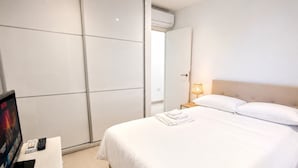 Hotellihuone, jossa on sänky, yöpöytä, jossa on televisio, kaukosäädin ja tabletti.