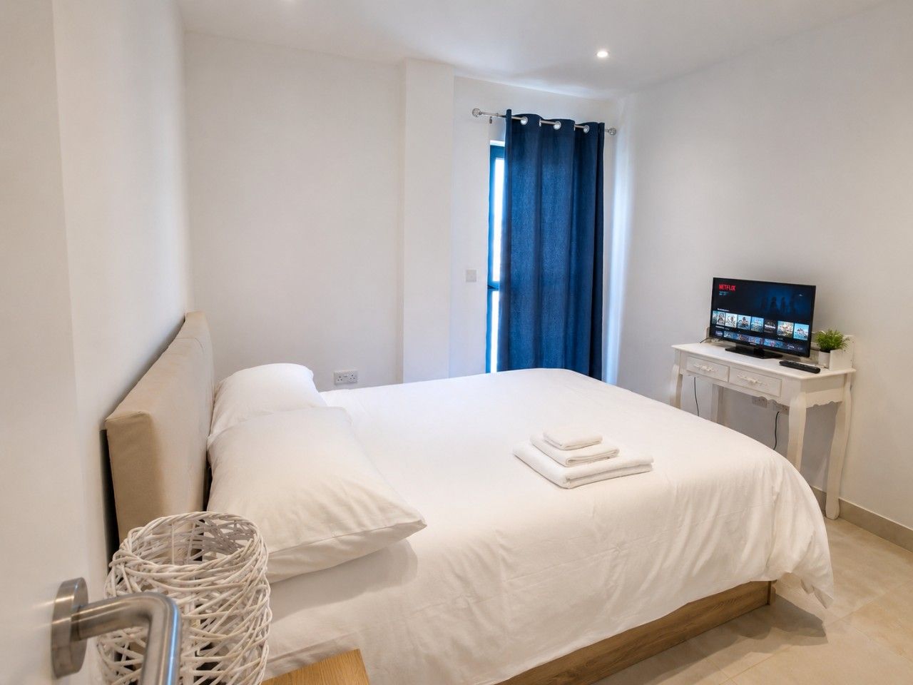 A hotel room with a bed, a TV, and a window with curtains.