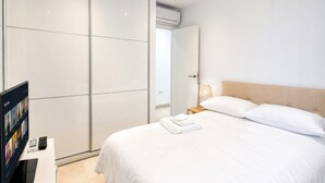 Hotellihuone, jossa on sänky, yöpöytä lampun kanssa, televisio ja vaatekaappi.