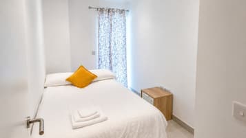 A hotel room with a bed, a nightstand, a window with curtains, and a door.