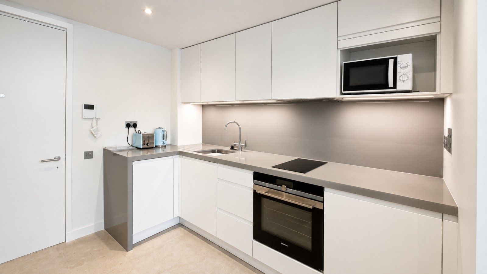 Een moderne keuken met witte kastjes, een ingebouwde magnetron, een vaatwasser en een spoelbak.