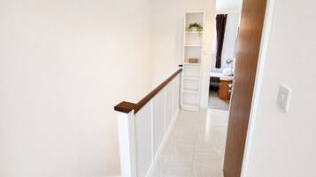 A staircase with white walls and wooden handrails leading to a room with a bed, a nightstand, and a shelf with a plant.