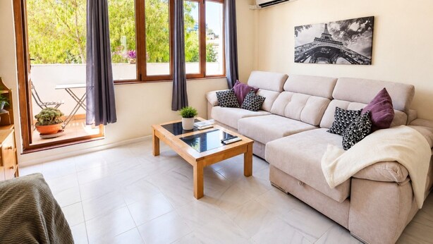 Uma sala de estar com sofá, mesa de centro e uma janela grande com cortinas.