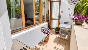Um pátio externo com mesa e cadeiras, um vaso de planta e uma porta de correr de vidro que dá para um espaço interno.