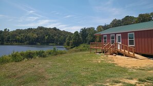 Uma cabana com varanda, um lago e colinas arborizadas ao fundo.