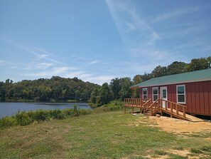 A cabin with a deck, a lake, and forested hills in the background. - The Yellow Rose- Lakehouse at Arc Ridge Ranch Resort (Ben Wheeler)