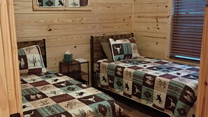 Uma cabana com duas camas de madeira, cada uma com colcha acolchoada com motivos de animais e padrões geométricos.