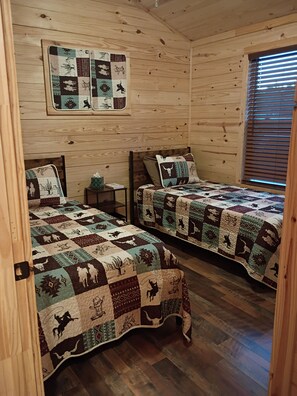 A cabin with two wooden beds, each with a quilted bedspread featuring animal and geometric patterns. - The Yellow Rose- Lakehouse at Arc Ridge Ranch Resort (Ben Wheeler)