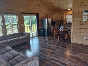 A wooden interior with a sofa, dining table, chairs, and a refrigerator. - The Yellow Rose- Lakehouse at Arc Ridge Ranch Resort (Ben Wheeler)