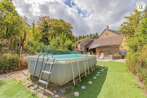 Ein Pool im Freien mit einer Leiter, umgeben von einer Rasenfläche mit trittsteinförmigen Pfaden, und ein Steinhaus im Hintergrund.