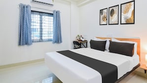 Une chambre d’hôtel avec un grand lit, un bureau avec une chaise, une fenêtre avec des rideaux et des œuvres d’art murales.