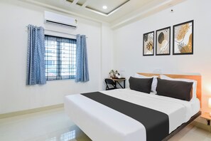 A hotel room with a large bed, a desk with a chair, a window with curtains, and wall art. - Super Townhouse Kokapet Formerly Aarian (Hyderabad)