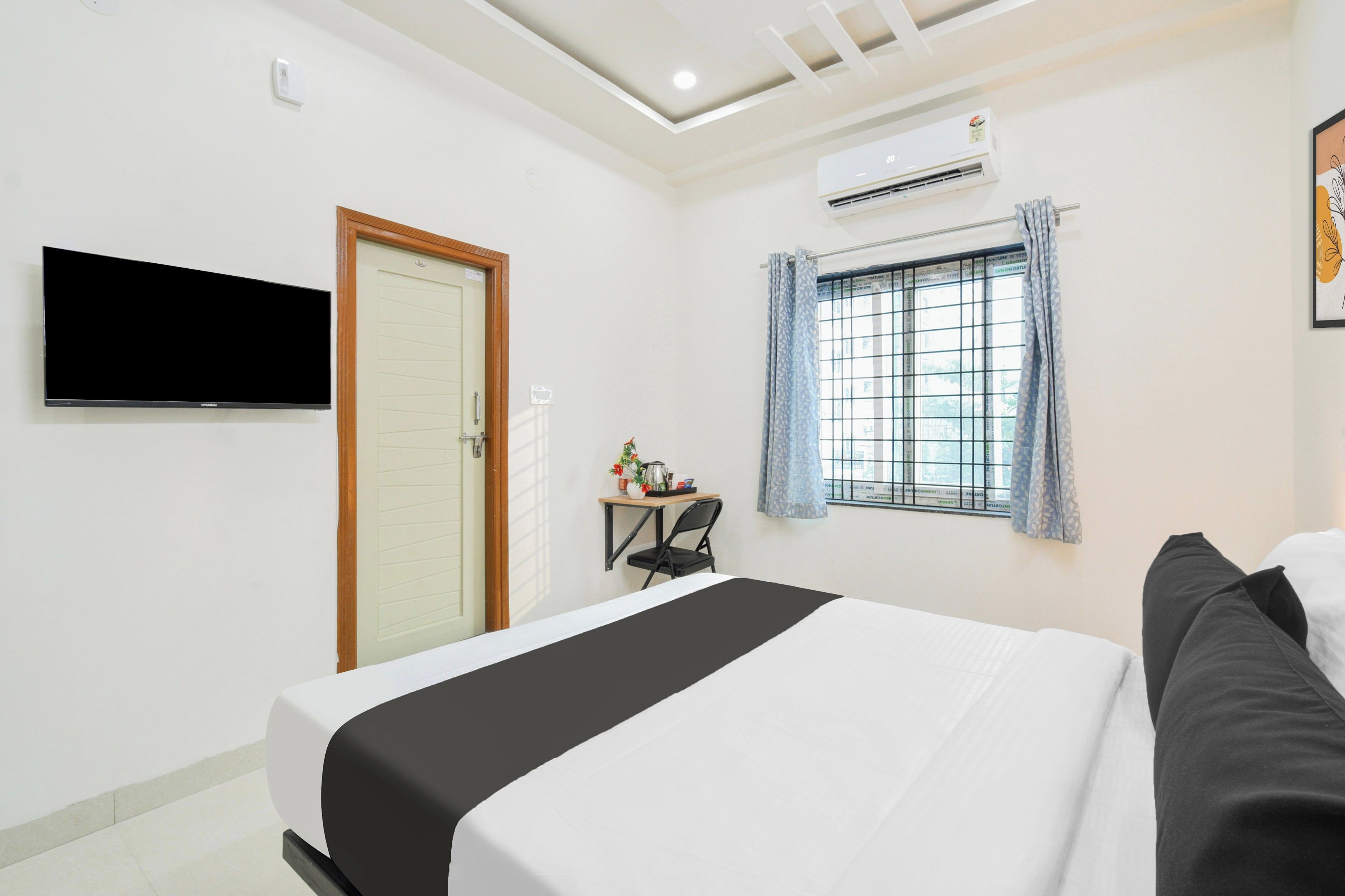 A hotel room with a bed, a television, a window with curtains, and an air conditioning unit.