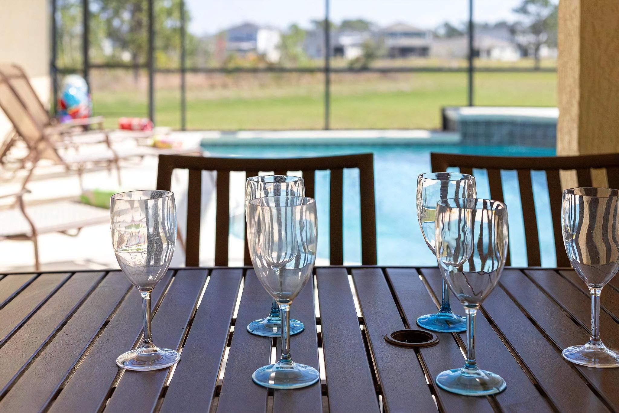 A table with empty wine glasses and a view of a swimming pool.