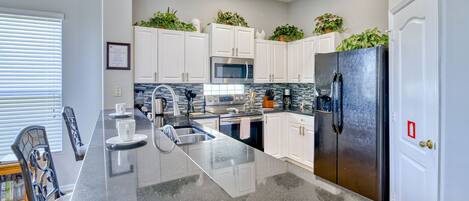 A modern kitchen with white cabinets, stainless steel appliances, and a granite countertop.