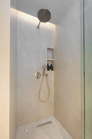 A shower with a handheld showerhead and a wall-mounted faucet. There are two bottles on a shelf above the shower.