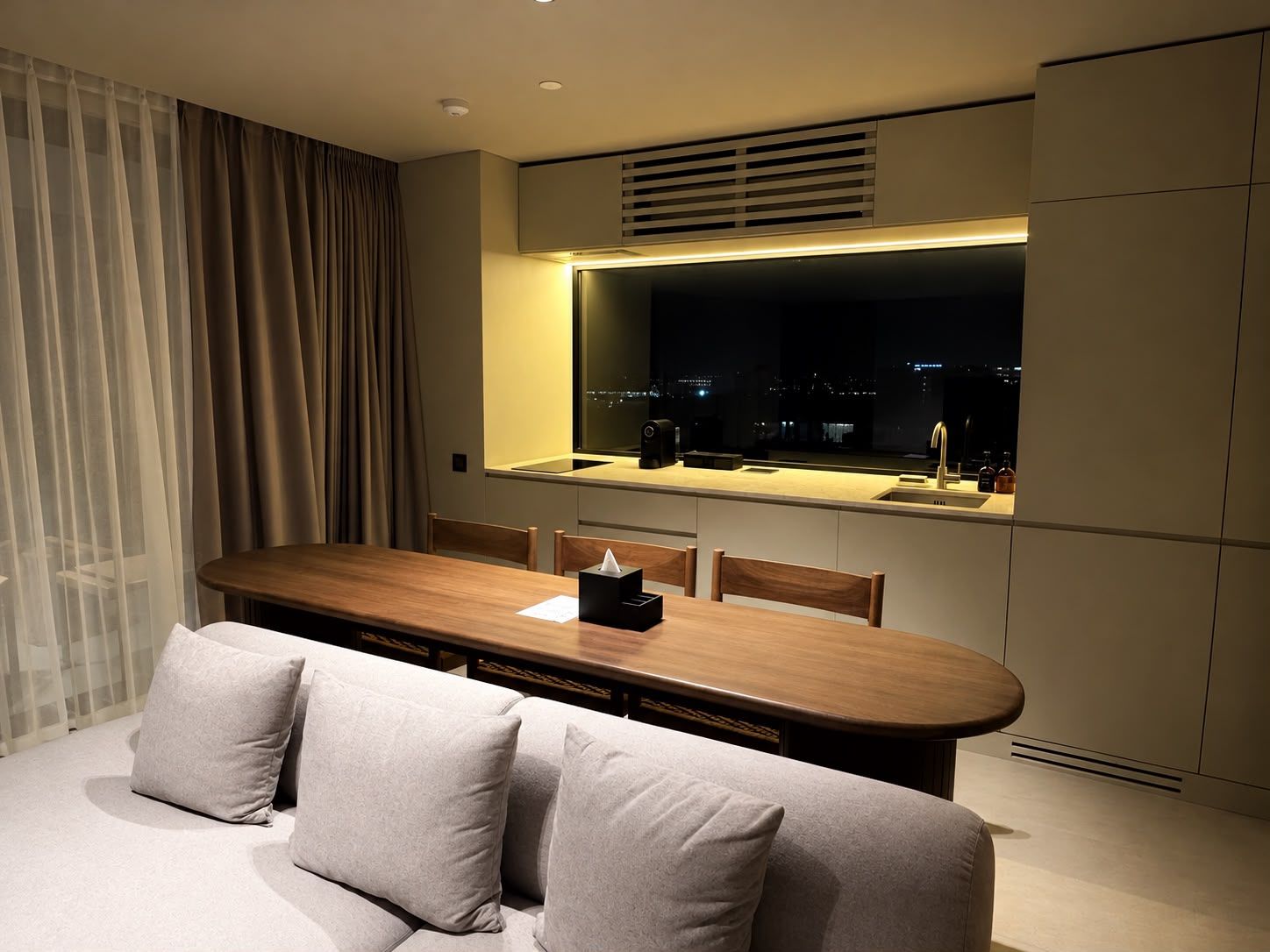 Habitación de hotel moderna con comedor, sofá y un amplio ventanal con vistas a la ciudad.