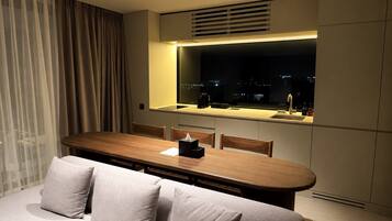 Habitación de hotel moderna con comedor, sofá y un amplio ventanal con vistas a la ciudad.