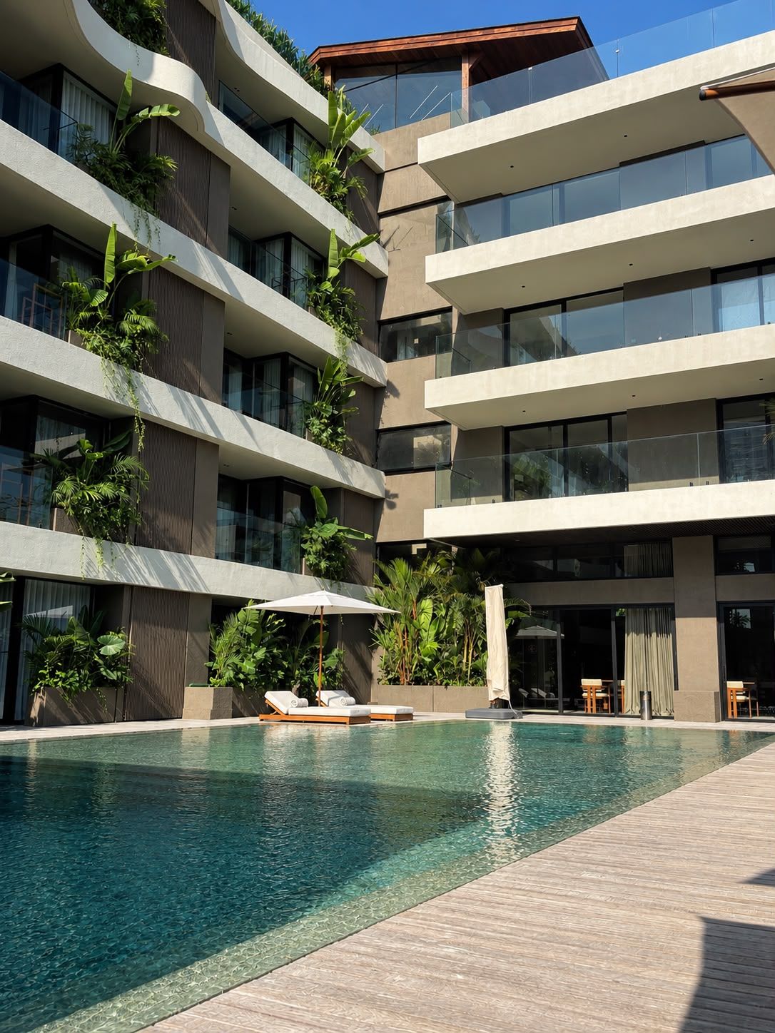 A modern hotel with a swimming pool, outdoor seating, and balconies with plants.