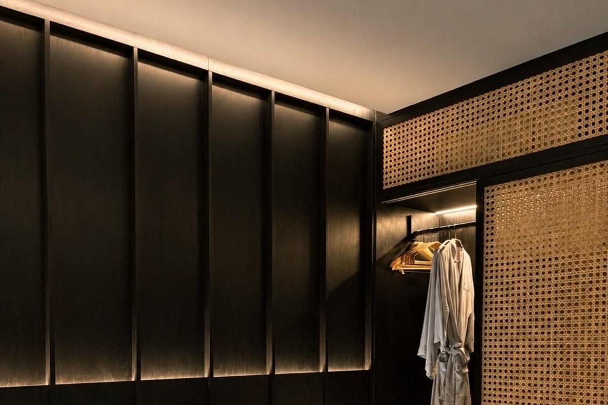 A hotel room with a bed, a nightstand, a lamp, a robe hanging on a rack, and a textured wall panel.