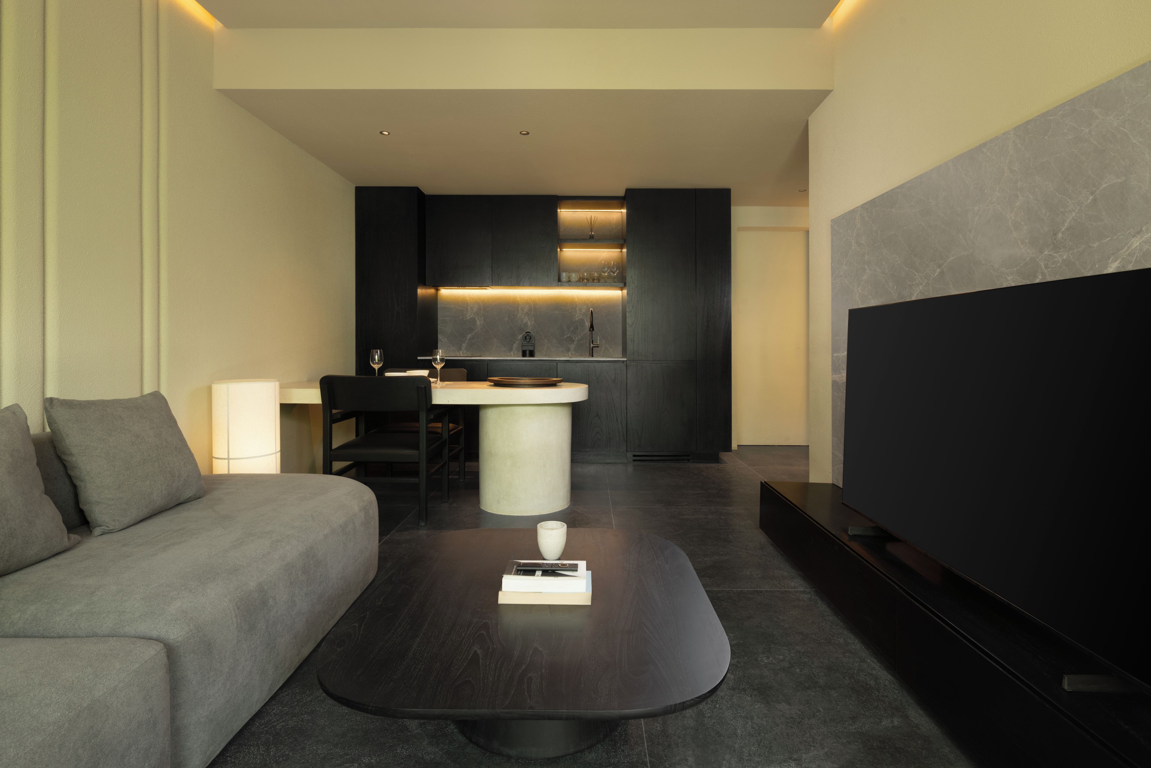 Una habitación de hotel moderna con sofá, mesa de centro, televisor y zona de cocina.