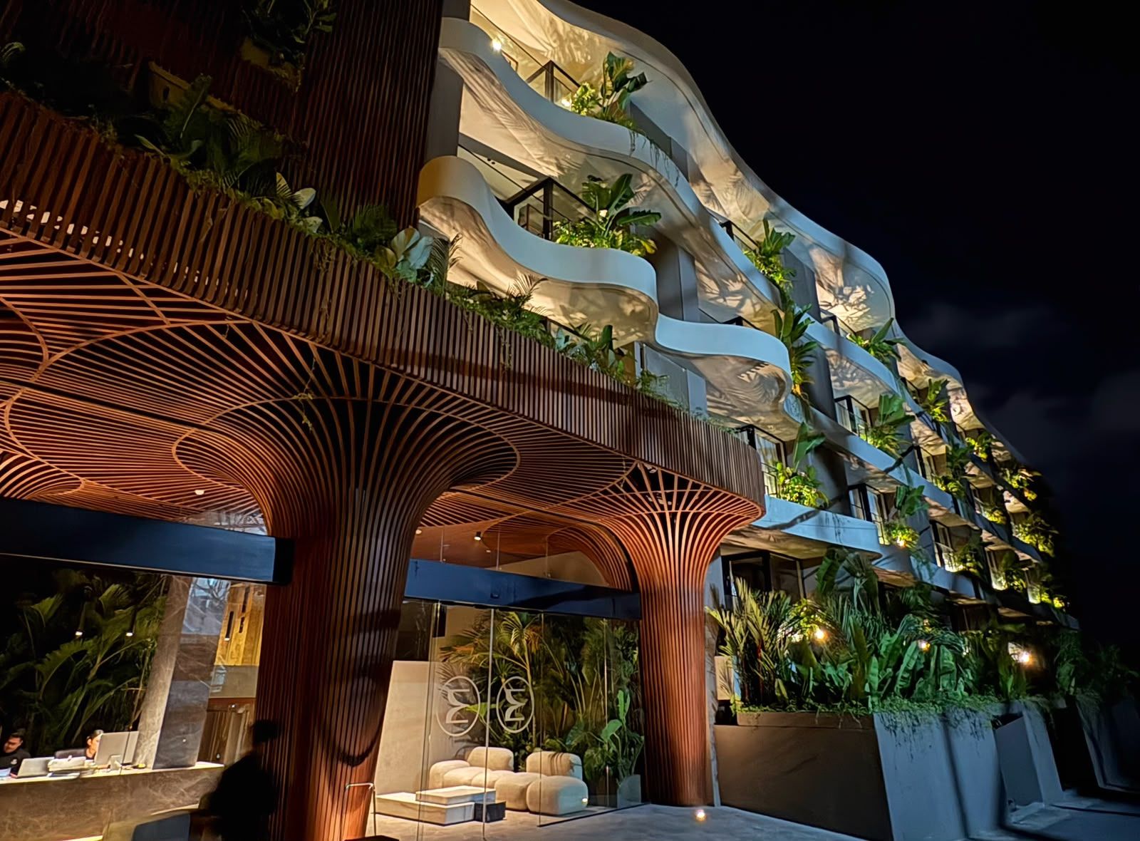 Un edificio moderno con fachada curva distintiva, zona de estar exterior e integración de vegetación en el diseño.