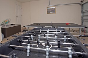 Ein Kicker in einem Raum mit einer weißen Tür, einem gerahmten Bild an der Wand und einem roten Schläger auf dem Tisch.