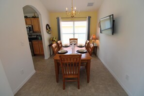 A dining area with a wooden table set for six, flanked by chairs, a chandelier, and a television on the wall. - Spacious 5 bed on Solana resort (Davenport)
