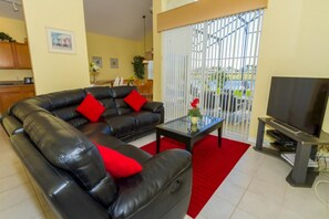 A living room with a black leather sofa, a glass coffee table, and a flat-screen TV. - Home With a View! (378106) (Kissimmee)