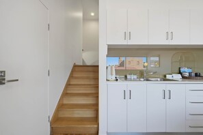 A modern kitchen with white cabinets, a wooden staircase, and a view of the outside. - Warwick 1 – Stylish Hobart Retreat (Hobart)