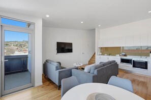 A modern apartment with a balcony, a living area with sofas, a kitchen with white cabinets, and a flat-screen TV mounted on the wall. - Warwick 1 – Stylish Hobart Retreat (Hobart)