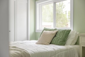 Un dormitorio con cama, ventana y mesita de noche.