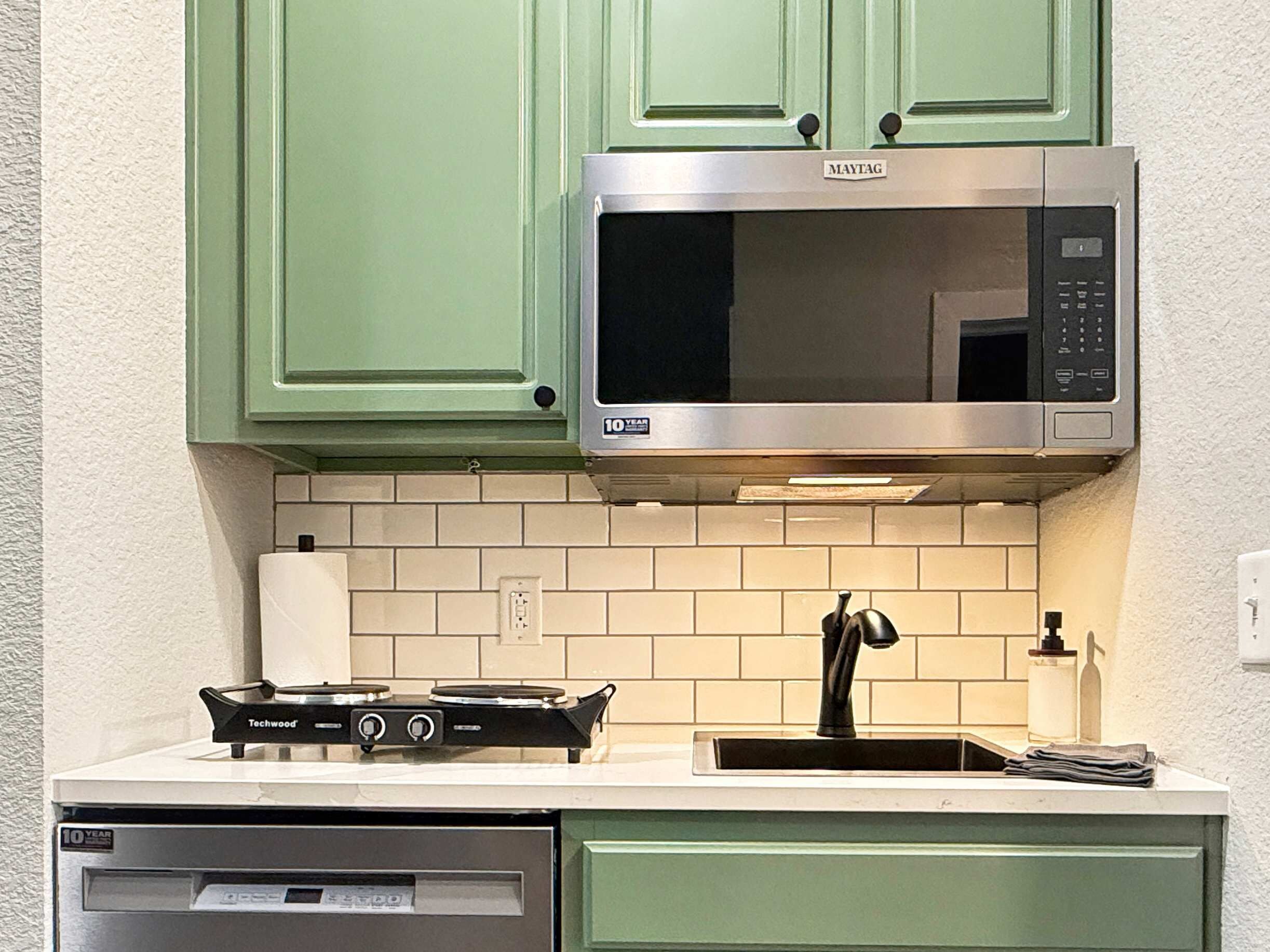A kitchen with green cabinets, a stainless steel microwave, a gas stove, and a dishwasher.