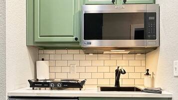 A kitchen with green cabinets, a stainless steel microwave, a gas stove, and a dishwasher.