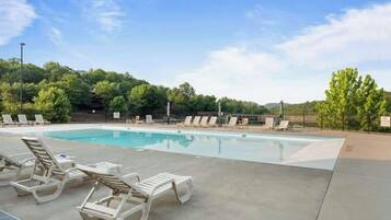 A swimming pool with lounge chairs, surrounded by trees and a clear sky.