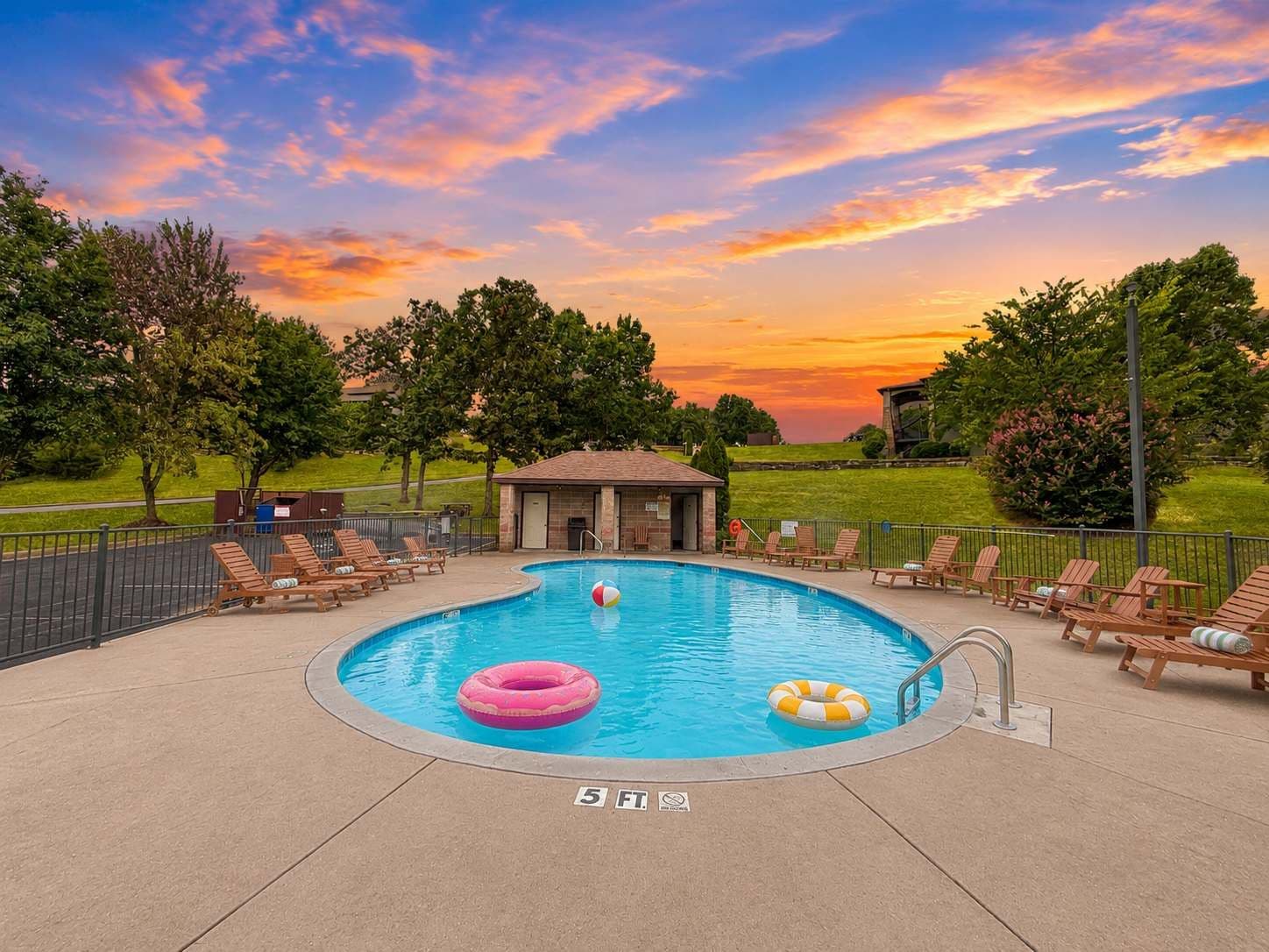 Une piscine circulaire entourée d’arbres, avec des chaises longues et un poste de surveillance pour les sauveteurs, offrant une vue imprenable sur le coucher du soleil.