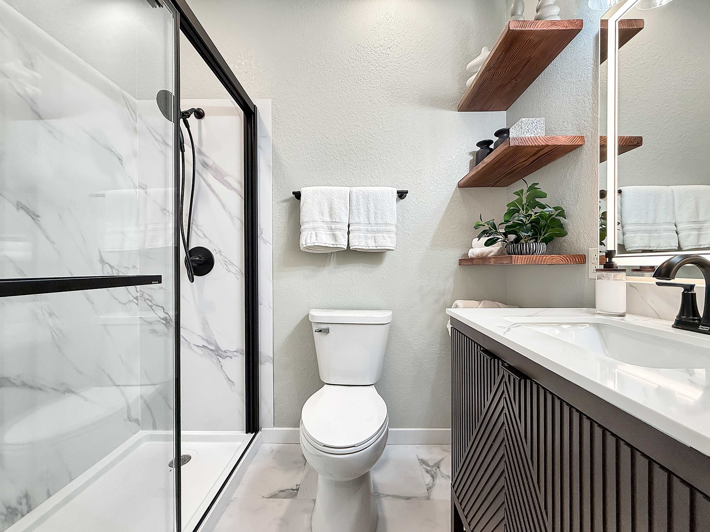 Une salle de bain moderne avec une douche à parois de verre, des toilettes blanches et un meuble-lavabo avec un miroir.